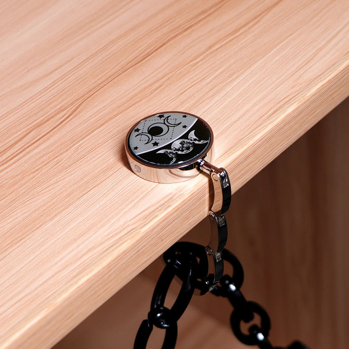 Silberner faltbarer Haken mit Monddesign, befestigt an einer hellen Holzoberfläche.