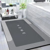 A modern gray anti-slip floor mat is displayed next to a white bathroom sink and a glass storage shelf.