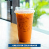 An orange iced drink in a clear plastic cup with a lid sitting on a wooden surface.