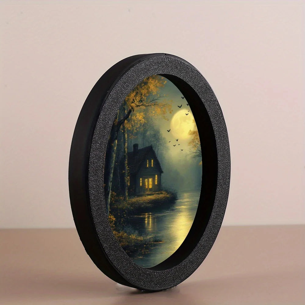A round, black photo frame with a glass cover displaying a moonlit forest scene with a house and birds.