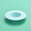 A white kitchen sink drain strainer and hair catcher with a perforated design, shown against a light green background.