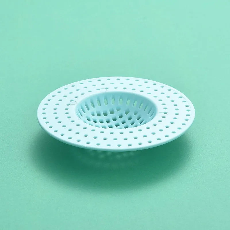 A white kitchen sink drain strainer and hair catcher with a perforated design, shown against a light green background.