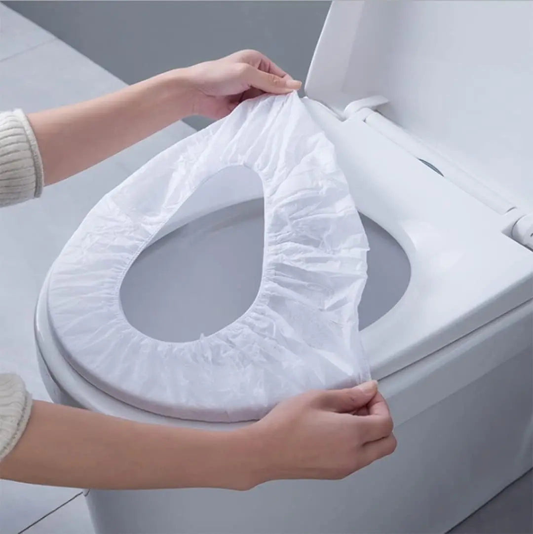 Hands are placing a white waterproof disposable toilet seat cover onto a white toilet bowl.