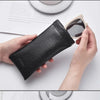 A hand holds a black PU leather squeeze eyeglasses case with soft lining next to a pair of sunglasses.