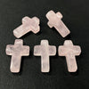 Three pink quartz cross pendant charms arranged on a dark surface.
