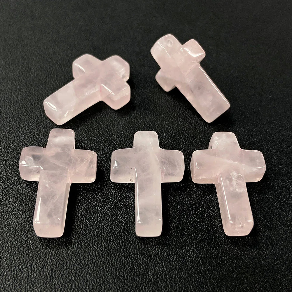 Three pink quartz cross pendant charms arranged on a dark surface.