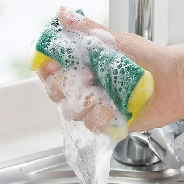 Eine Hand hält eine grün-gelbe Mikrofascheibe unter fließendem Wasser in einer Küchenspüle.