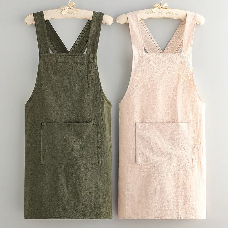 A pair of cotton kitchen aprons, one olive green and one pale pink, displayed on wooden hangers.