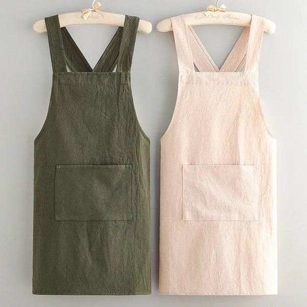 A pair of cotton kitchen aprons, one olive green and one pale pink, displayed on wooden hangers.