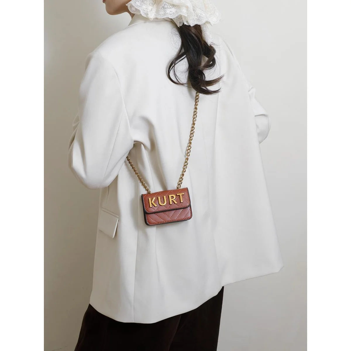 A white blazer worn by a person, featuring a brown leather magnetic crossbody bag with a letter flap chain.