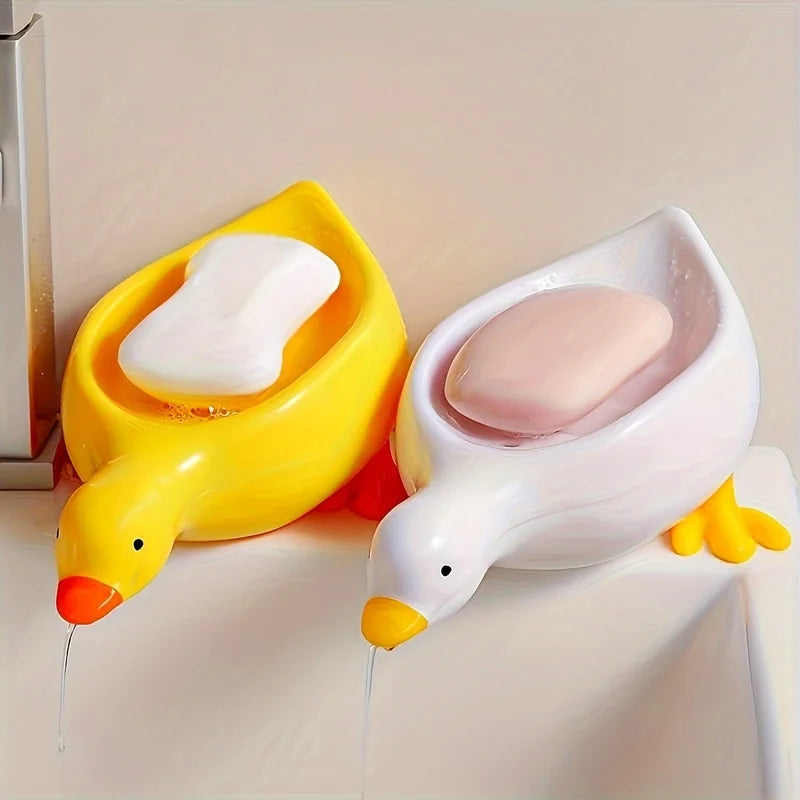 A yellow and white duck shaped soap dish with a self-draining tray is shown on a white surface.