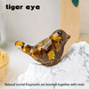 A golden-brown glass bird statue made of natural crystal fragments and resin resting on a white stone surface.