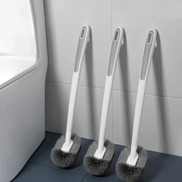 A white wall-mounted toilet brush with an ergonomic long handle is shown against a gray tiled wall.