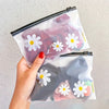 A hand holds a clear plastic zipper storage bag featuring a white daisy pattern.