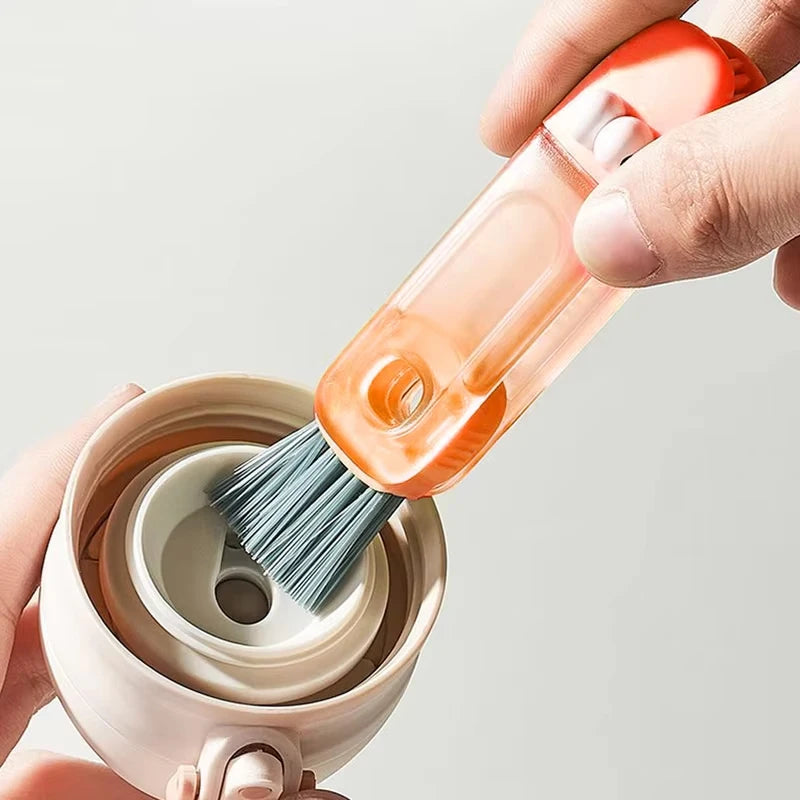 A hand holds an orange cleaning brush set with a wooden handle and bristles, positioned above a light-colored container.