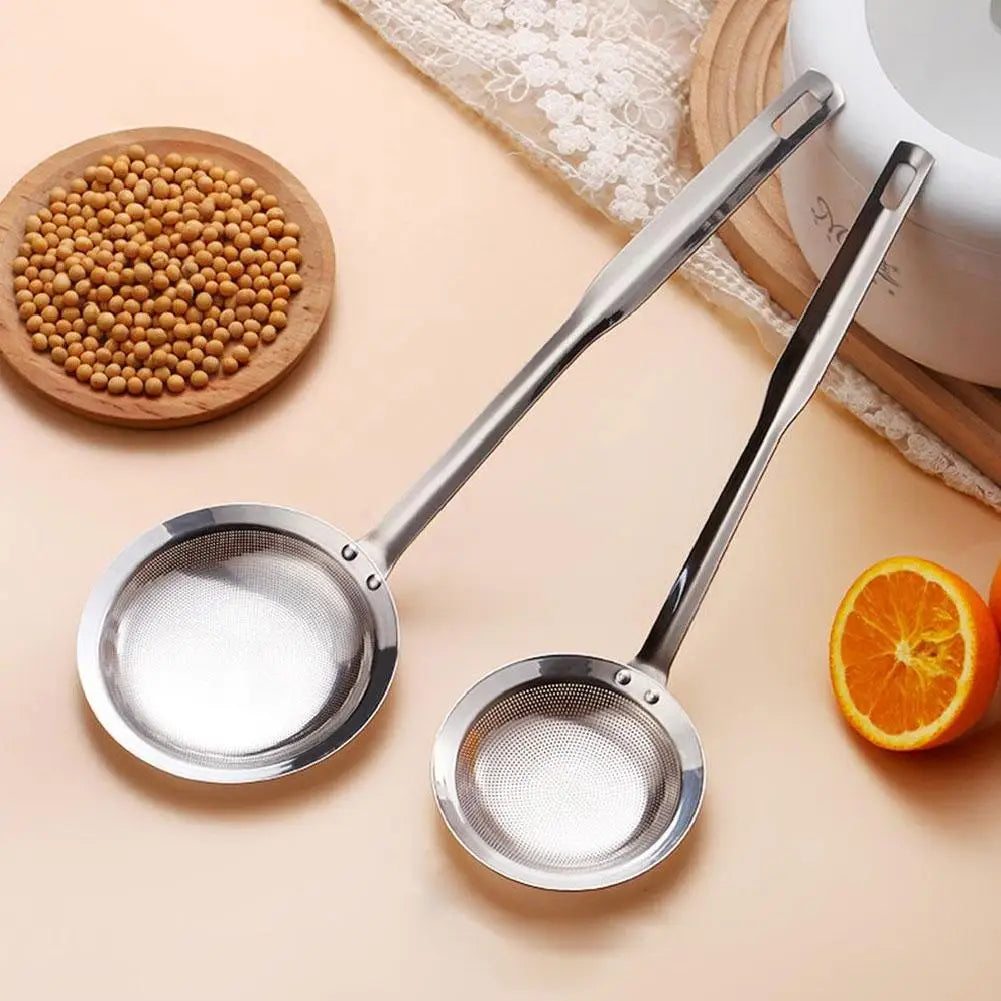 Stainless steel fat skimmer strainer tool with a long handle and a wide bowl, next to whole coriander seeds.
