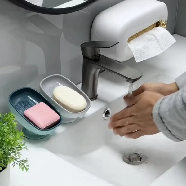 A hand is using a leaf-shaped bathroom soap dish drainer on a white sink.