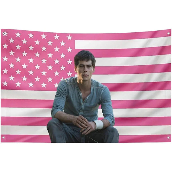 A man wearing a gray shirt stands in front of a pink and white striped flag tapestry.