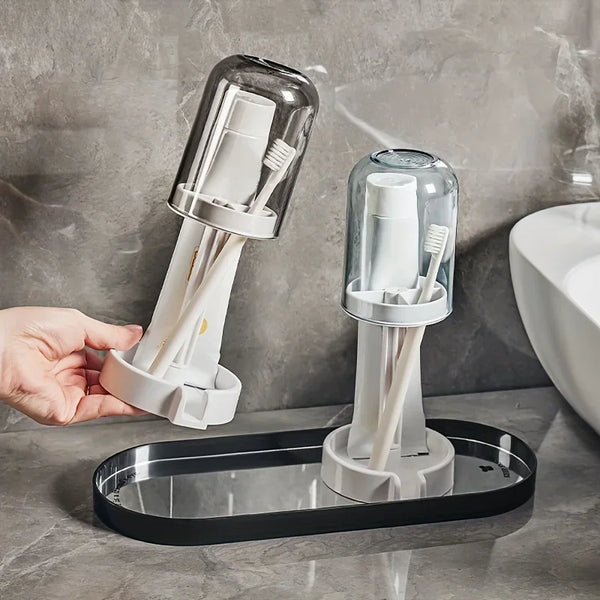A clear glass toothbrush holder with multiple compartments and a brush is displayed on a black tray.