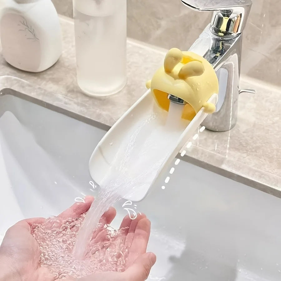 A hand is using an anti-splash faucet extender with a cute yellow rabbit design to dispense water into a sink.