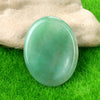 A smooth, translucent green quartz thumb stone resting on vibrant green grass.