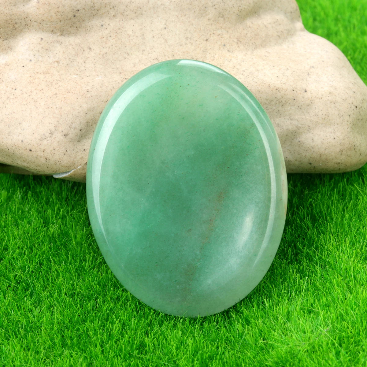 A smooth, translucent green quartz thumb stone resting on vibrant green grass.