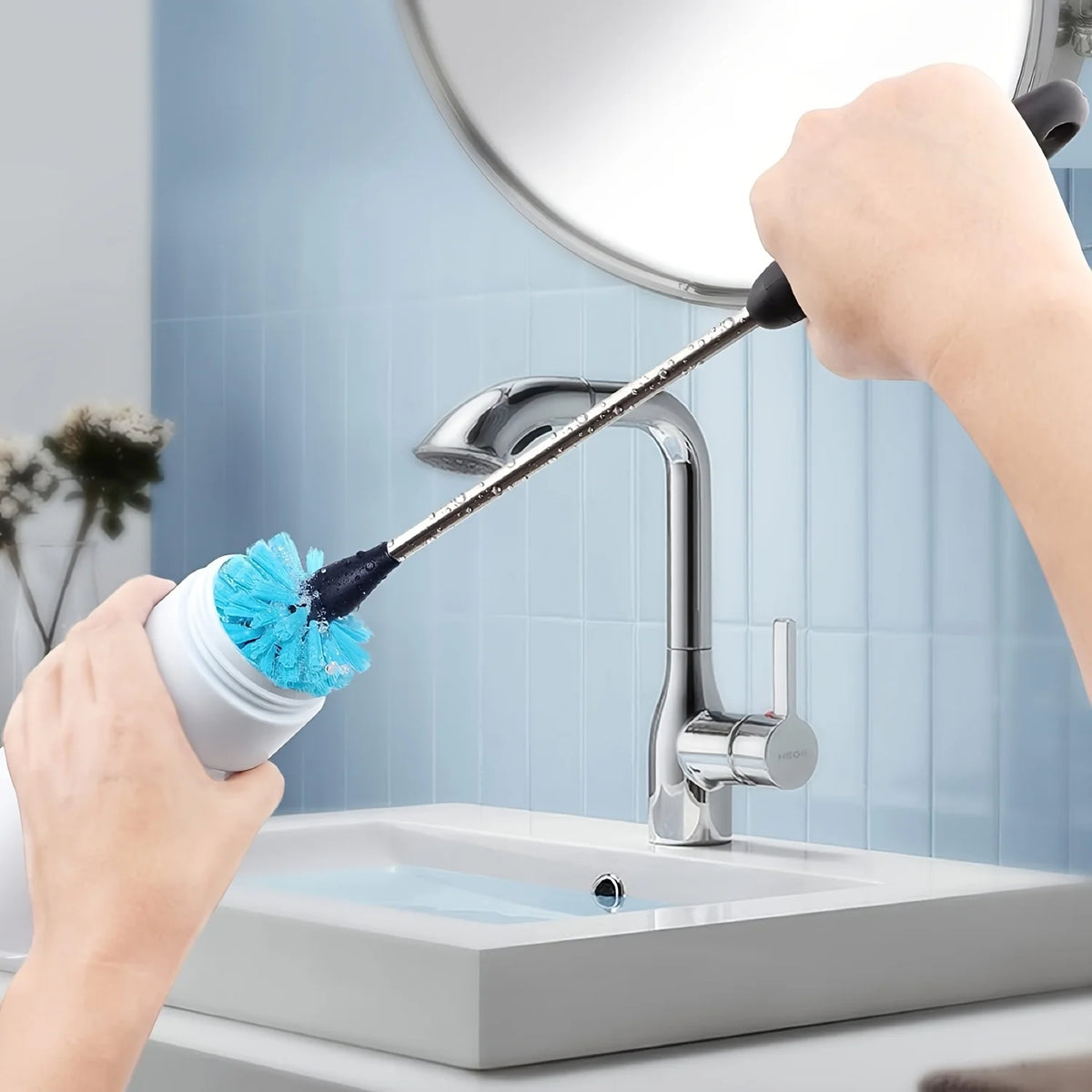 A hand is using a long-handled bottle brush set with stainless steel bristles to clean a kitchen faucet.