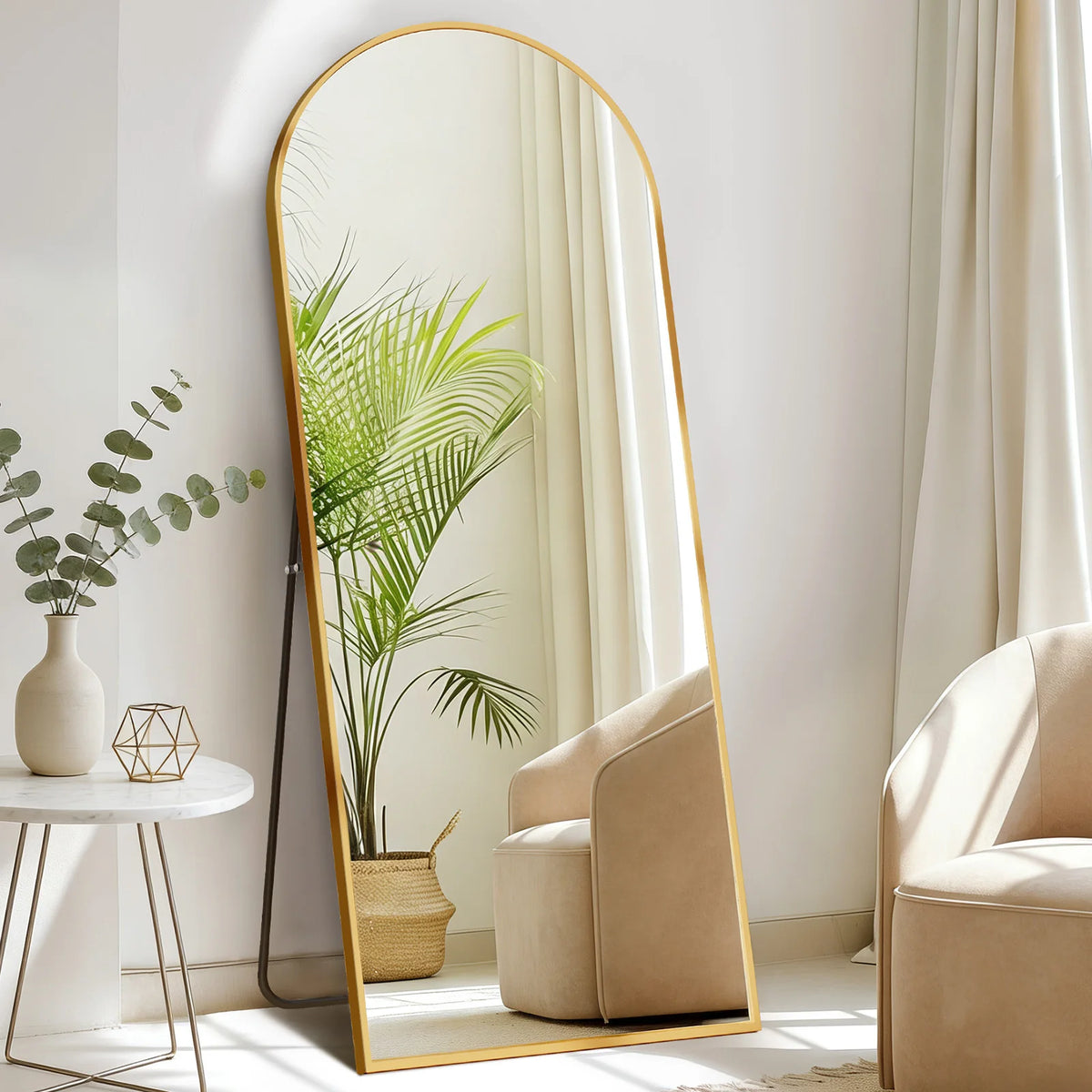 Ein vollflächiger Spiegel mit goldgerahmtem Rahmen reflektiert eine Topfpalme in einem hellen, modernen Interieur.