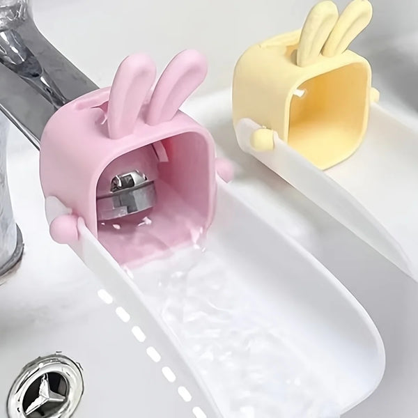 A pink anti-splash faucet extender with a rabbit design is shown dispensing water into a white dish.