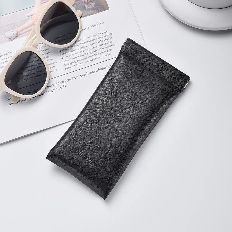 Black PU leather squeeze eyeglasses case with soft lining resting on a white surface.