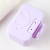 A purple ceramic soap dish with a lid featuring a smiling face, shown on a white surface.