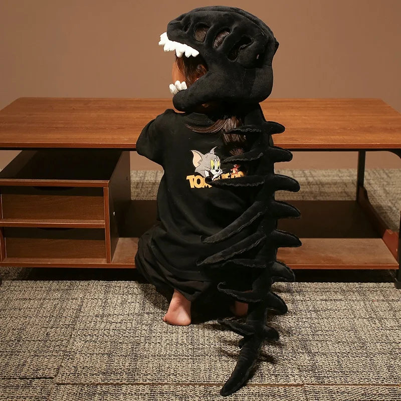 A person wearing a realistic dinosaur skeleton costume set with black fabric and white teeth, sitting in front of a wooden ta