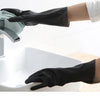 A hand wearing a black rubber cleaning glove is shown washing a dish under a faucet in a white sink.