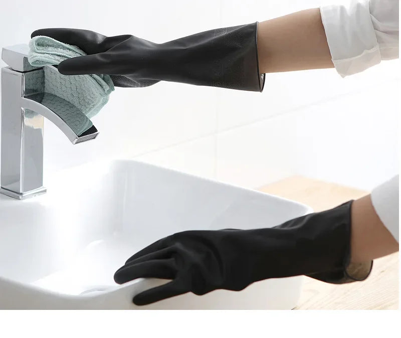 A hand wearing a black rubber cleaning glove is shown washing a dish under a faucet in a white sink.