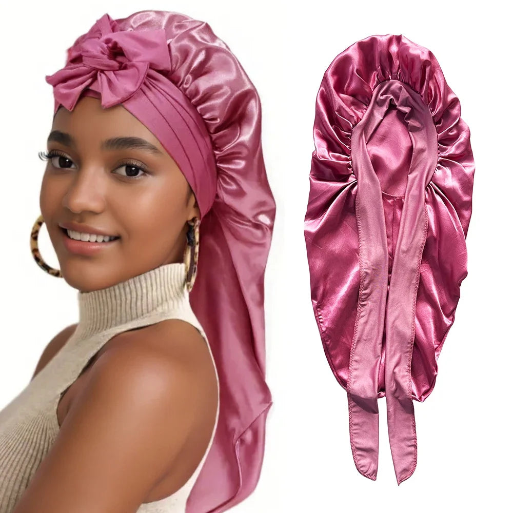 A woman models a satin sleeping bonnet in pink, featuring a large bow and gathered fabric.