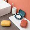 A portable travel soap box in orange and yellow colors is shown next to a toothbrush on a white surface.