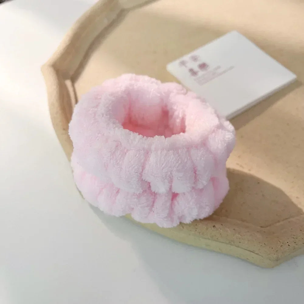 A pink microfiber wrist sweatband set for face washing and skincare resting on a light wooden tray.