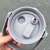 A hand holds a gray stainless steel insulated tumbler with a handle and straw.