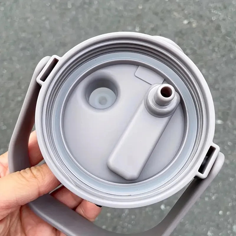 A hand holds a gray stainless steel insulated tumbler with a handle and straw.