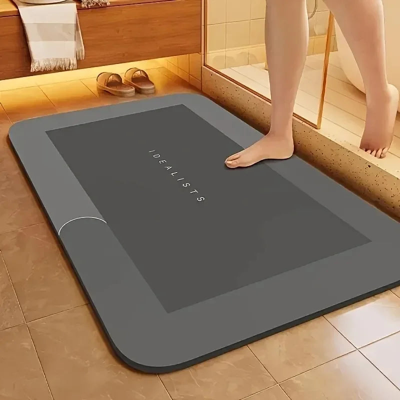 A gray diatomaceous earth absorbent bath mat is placed on a tiled floor next to a wooden cabinet.