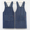 A pair of dark blue striped denim aprons hanging on a hanger.