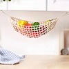 A macrame hanging fruit hammock filled with colorful fruits is displayed on a wooden surface.