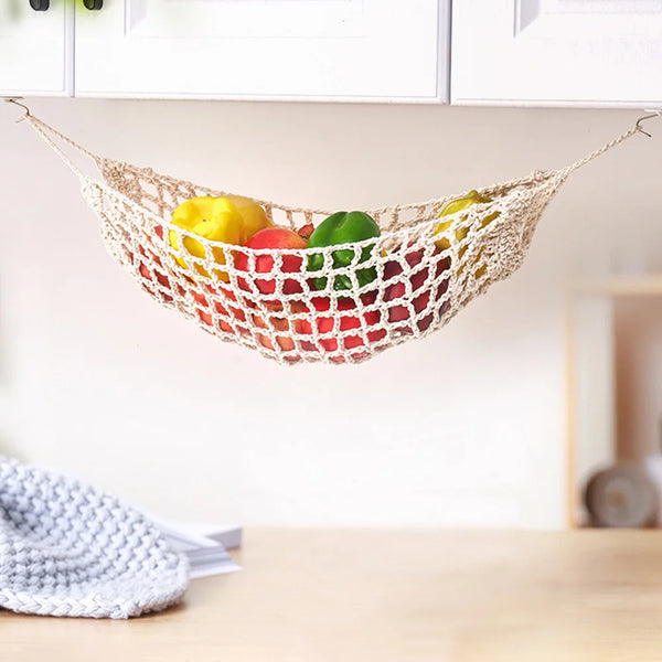 A macrame hanging fruit hammock filled with colorful fruits is displayed on a wooden surface.