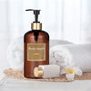 A brown pump dispenser bottle of body wash sits on a white surface next to a white soap bar and white towels.
