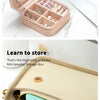 A light pink portable PU leather jewelry storage box with compartments filled with small silver and gold jewelry.