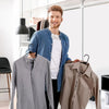 A man is standing in front of a large mirror, holding a gray shirt and a tan shirt, with plastic clothes hangers visible.