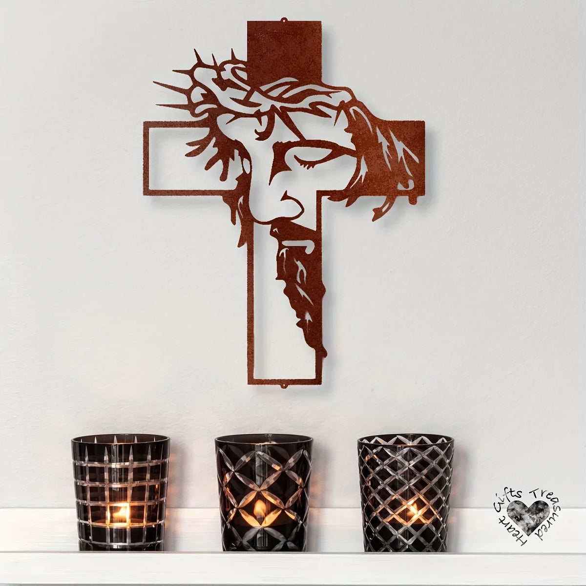 A rustic copper metal cross wall art decoration mounted on a white wall above three decorative candle holders.