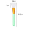 A white silicone facial mask brush with an orange handle and a light green base, shown next to a measurement scale.