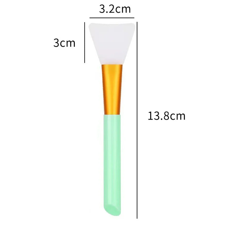 A white silicone facial mask brush with an orange handle and a light green base, shown next to a measurement scale.