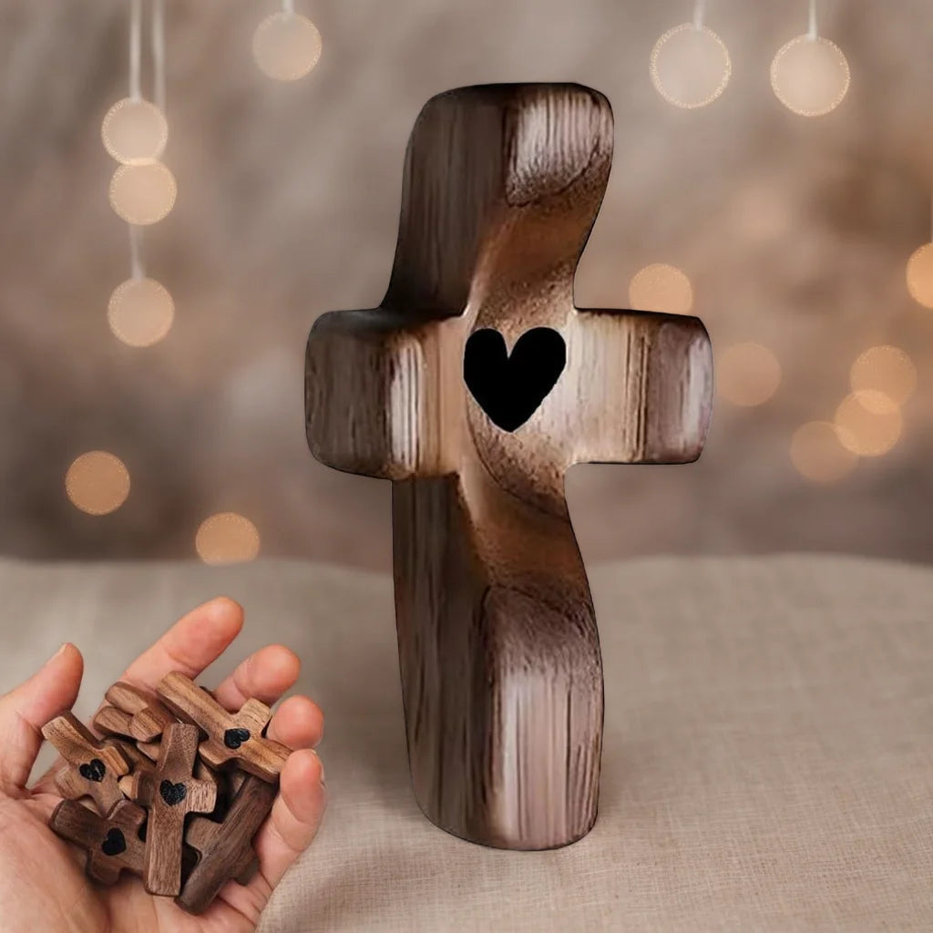 A handcrafted wooden cross with a heart cutout is displayed on a surface, next to a pile of small wooden crosses.